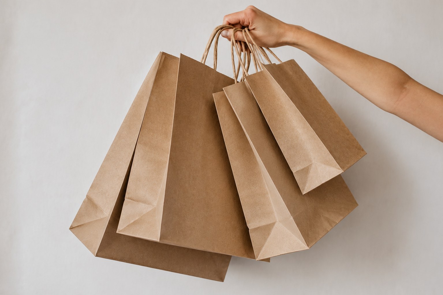 Hand holding a set of kraft paper shopping bags against a soft neutral wall